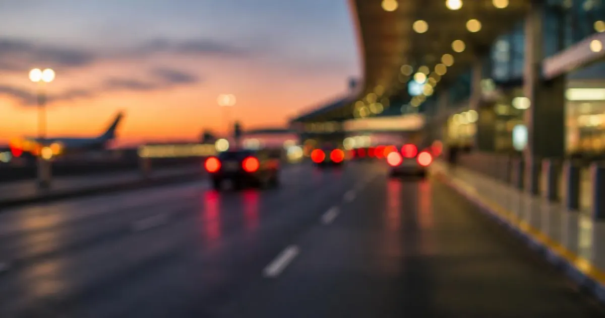 Luchthaven-oprit met een rij geparkeerde auto's in de schemering, onscherp