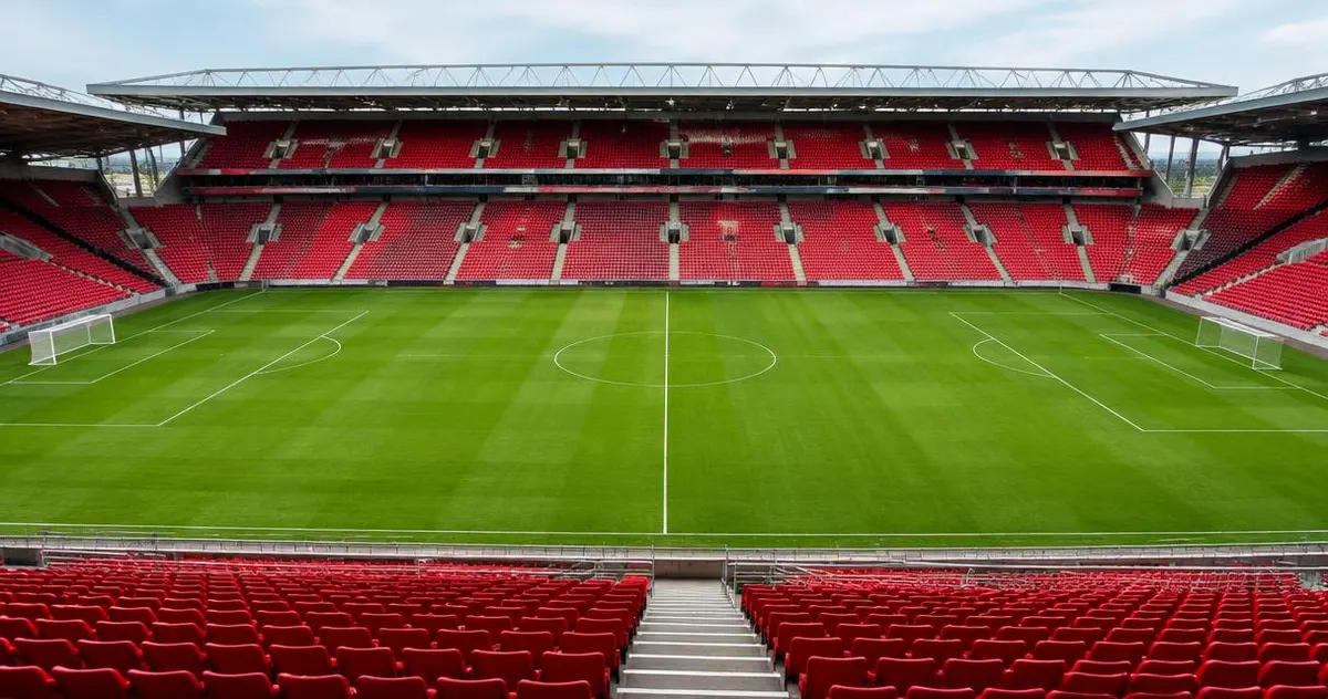 Empty football stadium with green pitch and red seats in daylight